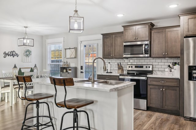 kitchen with tasteful backsplash, appliances with stainless steel finishes, a sink, dark brown cabinetry, and wood finished floors