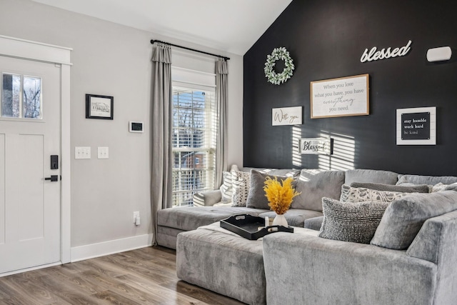 living room with vaulted ceiling, an accent wall, wood finished floors, and baseboards