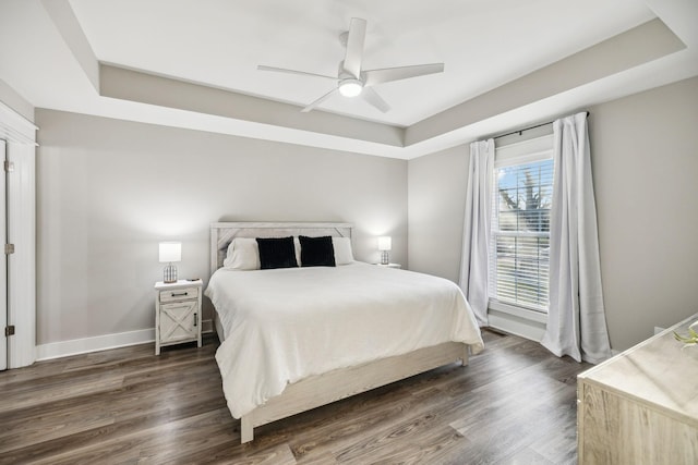 bedroom with baseboards, dark wood finished floors, a ceiling fan, and a raised ceiling