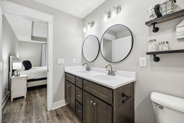 ensuite bathroom featuring double vanity, wood finished floors, a sink, and toilet