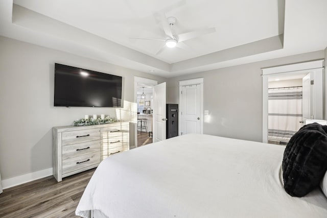 bedroom with a ceiling fan, baseboards, a tray ceiling, and wood finished floors