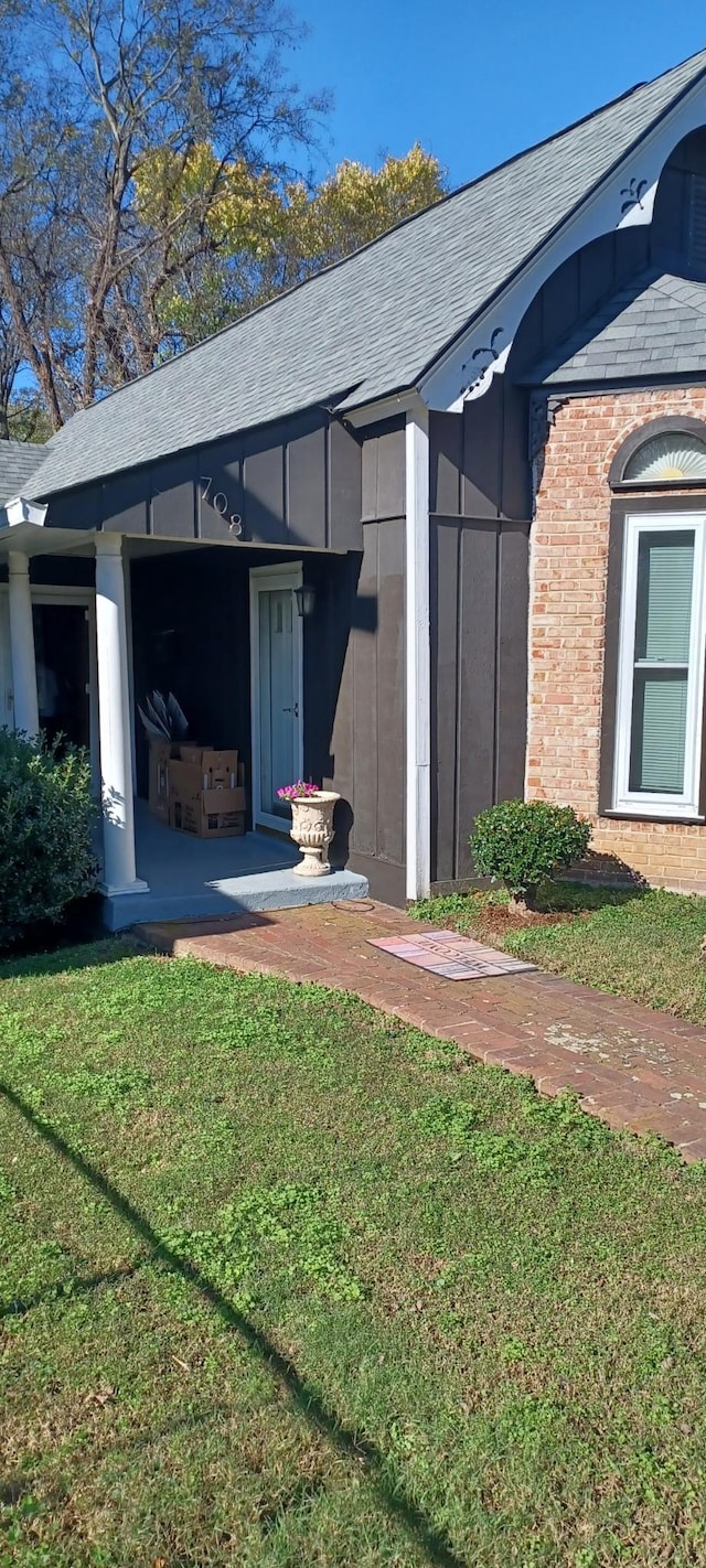 entrance to property with roof with shingles, a yard, and brick siding