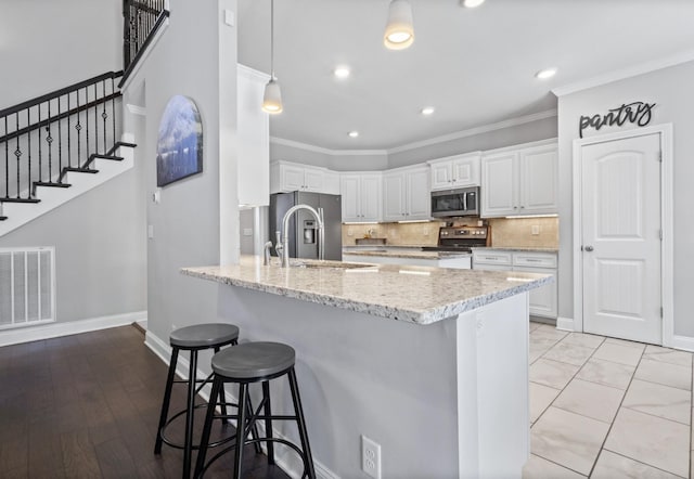 kitchen featuring visible vents, stainless steel appliances, crown molding, a kitchen bar, and a sink