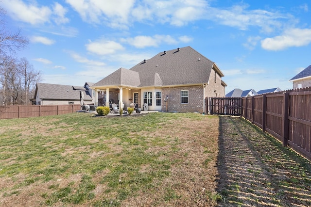 back of property with brick siding, a yard, roof with shingles, a patio area, and a fenced backyard