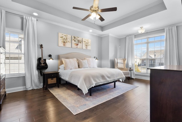 bedroom featuring ceiling fan, a tray ceiling, dark wood-type flooring, and baseboards