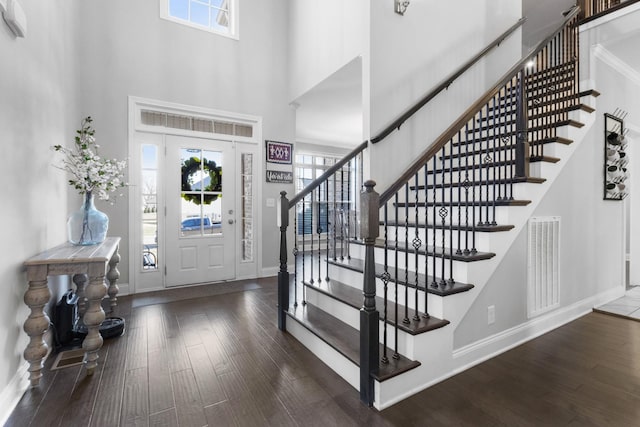 foyer entrance with baseboards, a high ceiling, visible vents, and wood finished floors