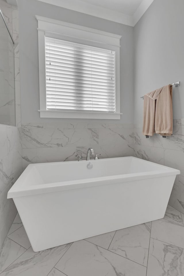 bathroom featuring a healthy amount of sunlight, marble finish floor, tile walls, and a soaking tub