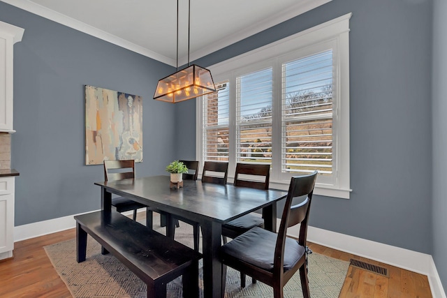 dining space featuring visible vents, crown molding, baseboards, and wood finished floors