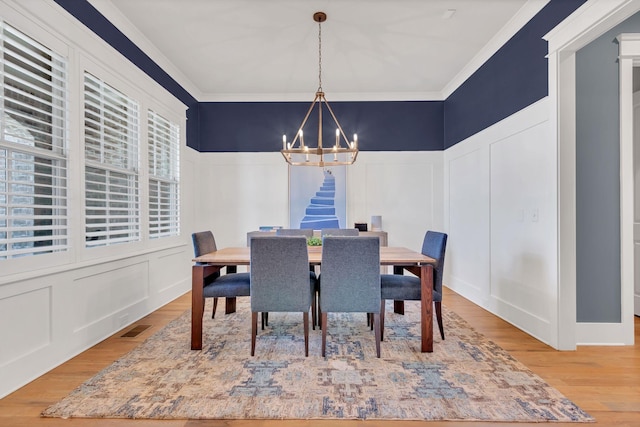 dining room featuring crown molding, a chandelier, a decorative wall, and wood finished floors