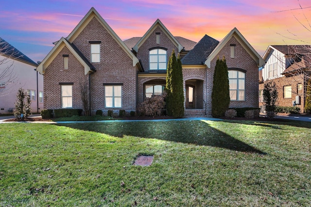 view of front facade with roof with shingles, brick siding, and a front lawn