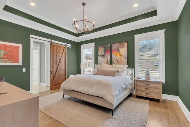 bedroom with a notable chandelier, a raised ceiling, a barn door, light wood-style floors, and baseboards