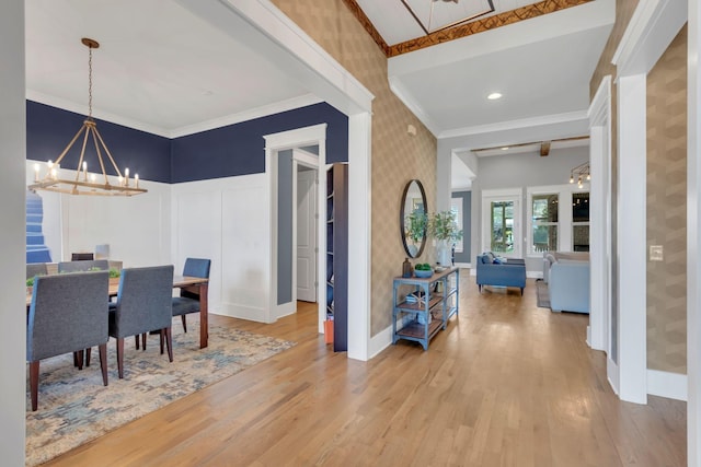 dining room with ornamental molding, wood finished floors, a notable chandelier, and wallpapered walls