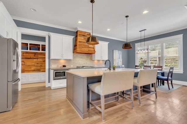 kitchen featuring a center island with sink, stainless steel appliances, tasteful backsplash, light wood-type flooring, and premium range hood