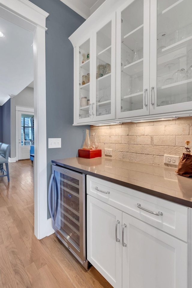 bar featuring a dry bar, beverage cooler, tasteful backsplash, baseboards, and light wood-style floors