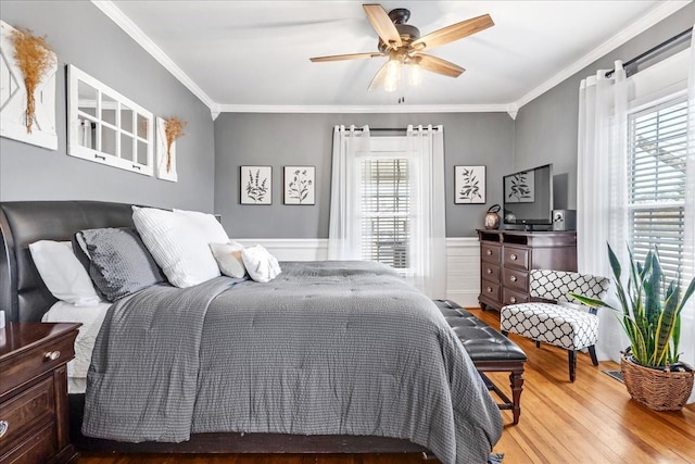 bedroom featuring a ceiling fan, ornamental molding, wood finished floors, and wainscoting