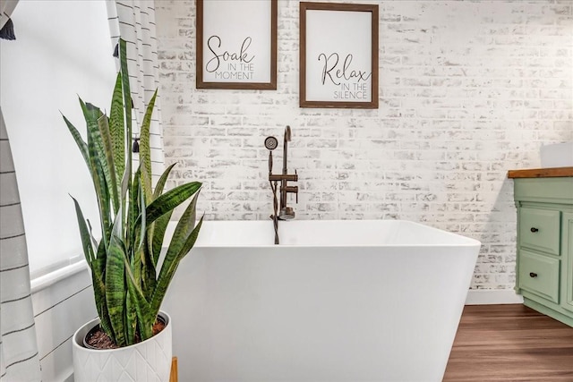 full bath featuring a freestanding tub, brick wall, and wood finished floors