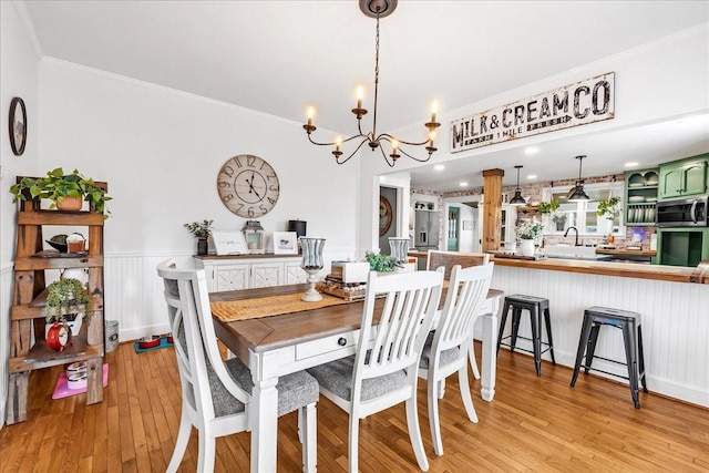 dining area featuring a notable chandelier, a wainscoted wall, light wood-style flooring, and crown molding