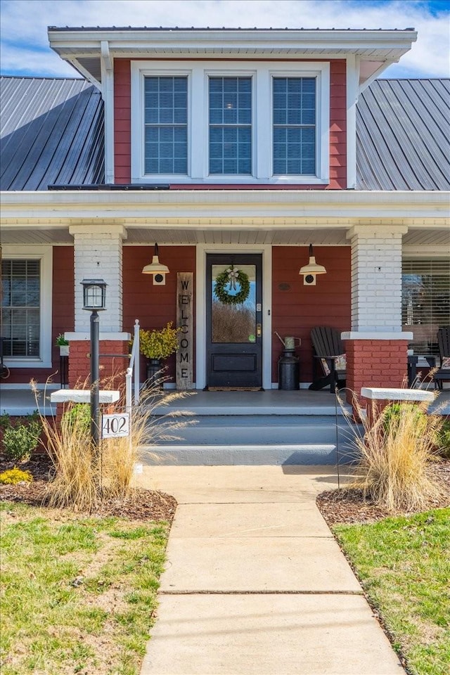 view of exterior entry with covered porch, brick siding, metal roof, and a standing seam roof