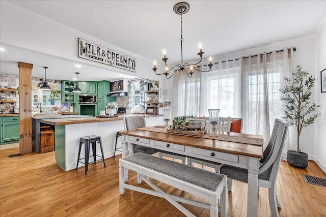 dining area with ornamental molding, light wood finished floors, visible vents, and a notable chandelier