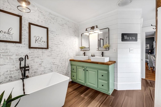 bathroom featuring a soaking tub, double vanity, a sink, and wood finished floors