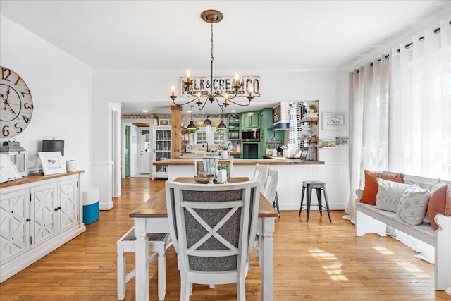 dining area with ornamental molding, light wood finished floors, and a chandelier