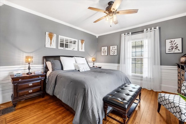 bedroom with a wainscoted wall, ornamental molding, visible vents, and hardwood / wood-style flooring