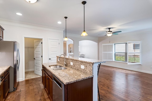 kitchen featuring arched walkways, ornamental molding, dark wood-type flooring, stainless steel appliances, and a sink