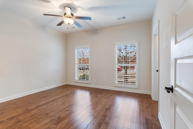 unfurnished room with ceiling fan, visible vents, baseboards, and dark wood finished floors