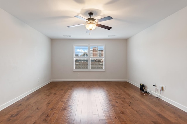 spare room featuring dark wood-type flooring, a ceiling fan, and baseboards