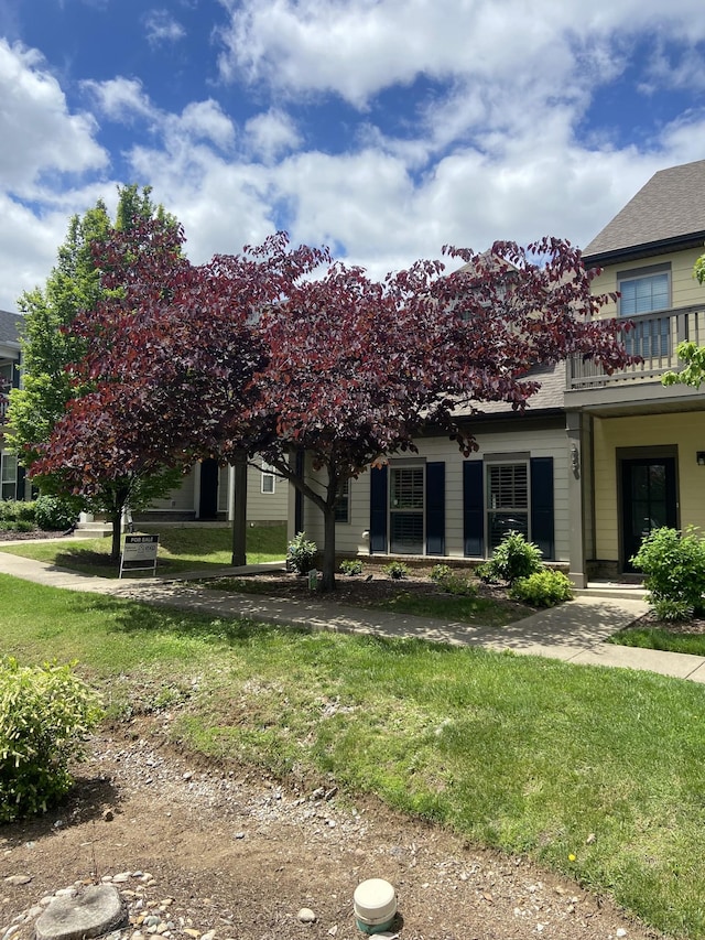 view of front of property featuring a front lawn, a balcony, and roof with shingles