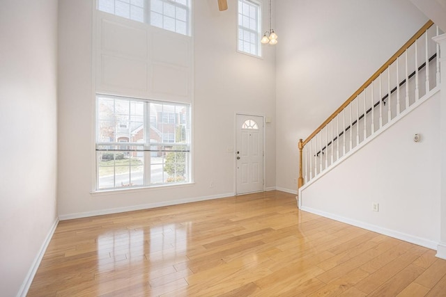 entrance foyer featuring stairway, baseboards, light wood-style flooring, and a towering ceiling