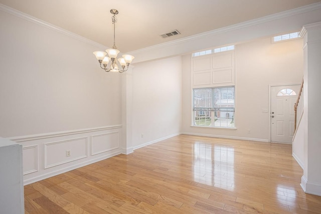 unfurnished room with light wood finished floors, a notable chandelier, a decorative wall, and crown molding