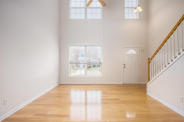 foyer with stairway, baseboards, light wood-style floors, and a towering ceiling