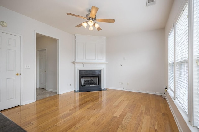 unfurnished living room featuring baseboards, visible vents, a fireplace with flush hearth, ceiling fan, and light wood-style floors