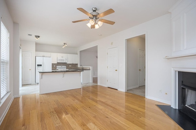 kitchen with light wood-style flooring, a fireplace with raised hearth, dark countertops, white appliances, and white cabinets