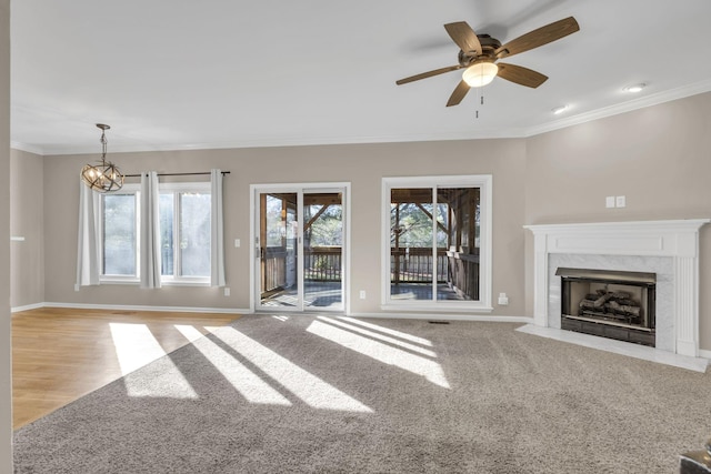 unfurnished living room featuring baseboards, a premium fireplace, ceiling fan with notable chandelier, and crown molding