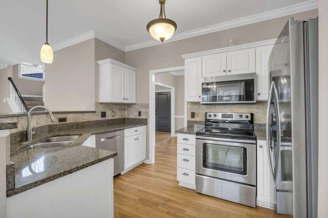 kitchen with stainless steel appliances, white cabinetry, a sink, dark stone countertops, and light wood-type flooring