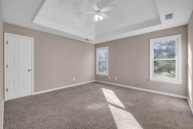 carpeted empty room with visible vents, a tray ceiling, and baseboards