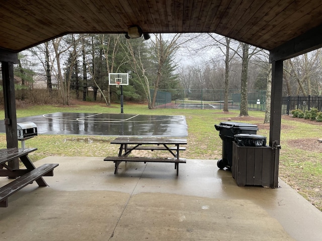 view of community featuring community basketball court, a lawn, fence, and a patio