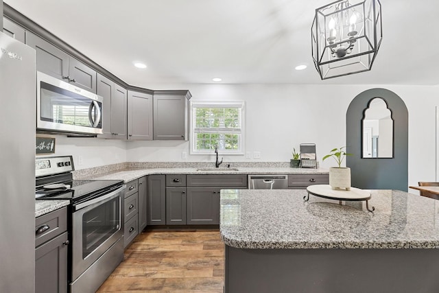 kitchen with stainless steel appliances, gray cabinets, light wood-type flooring, and a sink