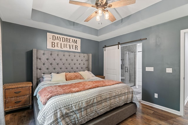 bedroom with ceiling fan, a barn door, wood finished floors, baseboards, and a tray ceiling