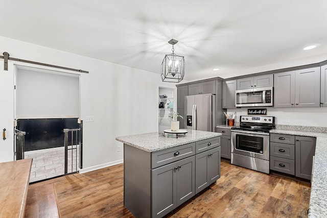 kitchen with a barn door, a kitchen island, wood finished floors, gray cabinets, and stainless steel appliances