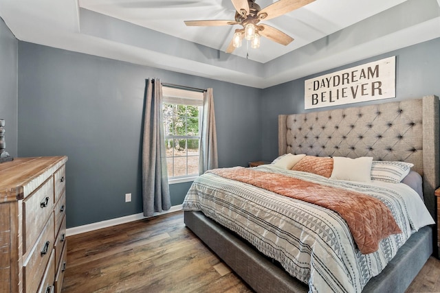 bedroom with dark wood-style floors, a raised ceiling, baseboards, and a ceiling fan