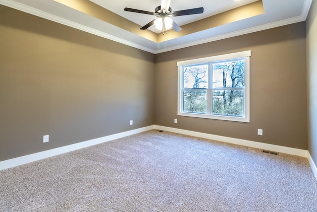 carpeted empty room featuring a raised ceiling, visible vents, ornamental molding, ceiling fan, and baseboards