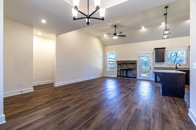 unfurnished living room featuring dark wood-style flooring, a sink, a stone fireplace, and ceiling fan with notable chandelier