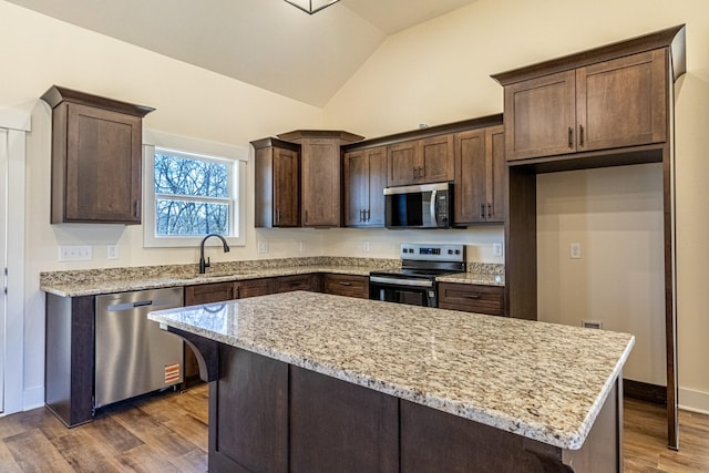 kitchen featuring dark wood finished floors, stainless steel appliances, vaulted ceiling, a sink, and dark brown cabinets