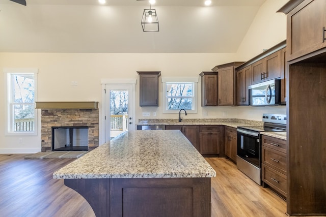 kitchen with a center island, a fireplace, stainless steel appliances, lofted ceiling, and a sink