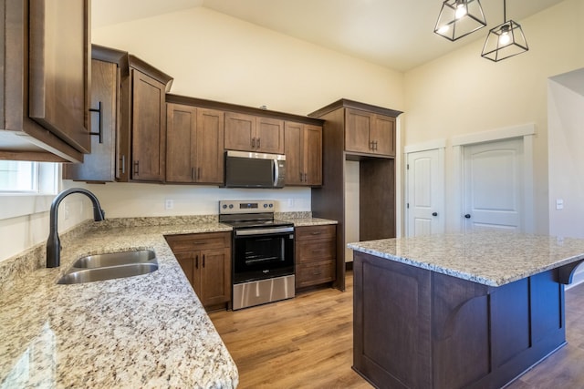 kitchen featuring light wood finished floors, appliances with stainless steel finishes, a sink, a kitchen island, and light stone countertops