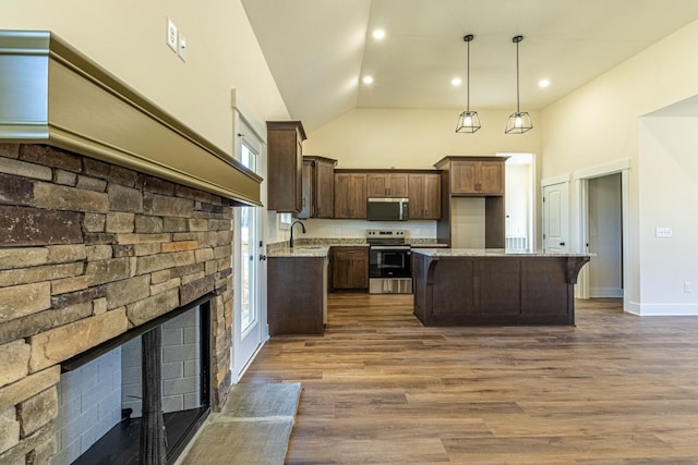 kitchen with dark wood finished floors, stainless steel appliances, a sink, dark brown cabinetry, and a kitchen island