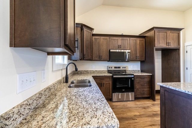 kitchen featuring light wood finished floors, light stone counters, stainless steel appliances, dark brown cabinets, and a sink